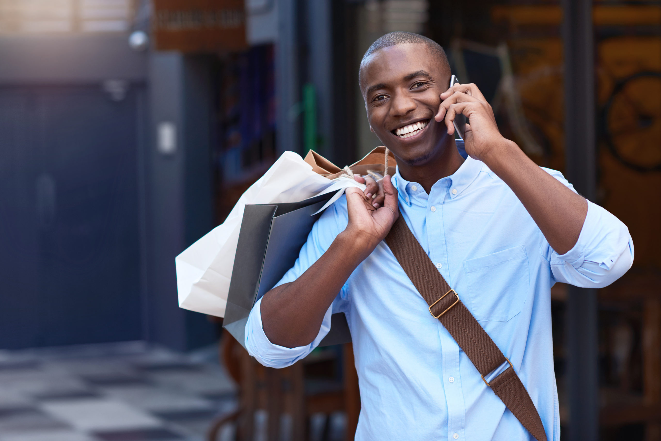 Smiling man carrying shopping bags talking on his cellphone outside
