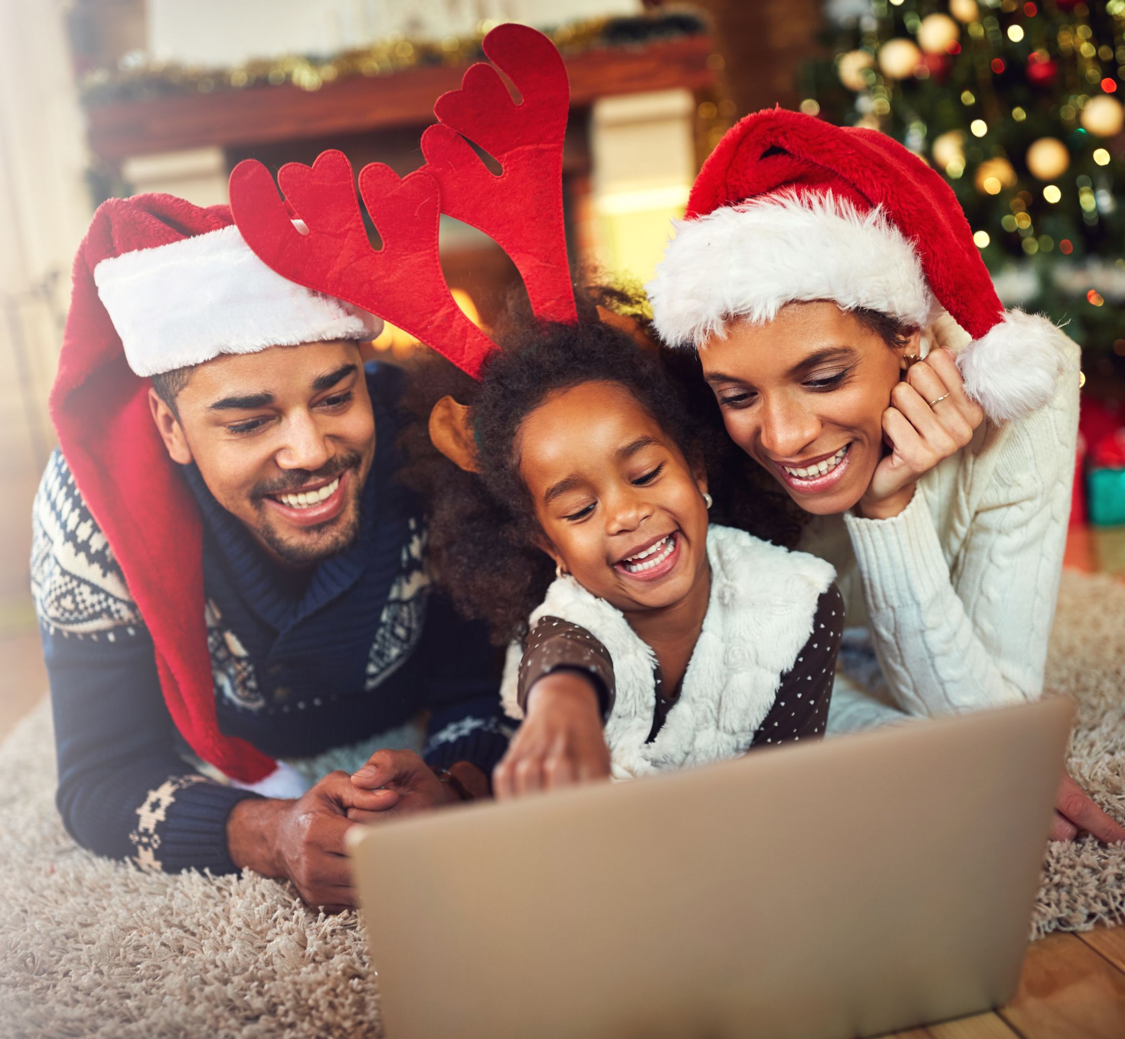Father, Mother, and daughter looking at a computer in holiday outfits.